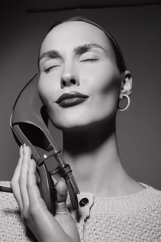 Closeup of a fair skinned European woman with closed eyes holding a shoe near her face, expressing calm and elegance in studio light.