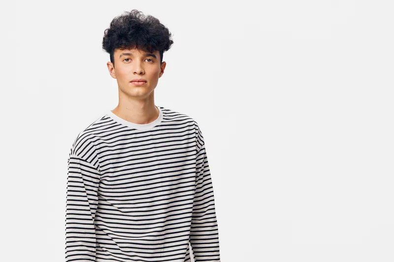 young man wearing striped shirt standing against white background with neutral expression and casual hairstyle in studio setting