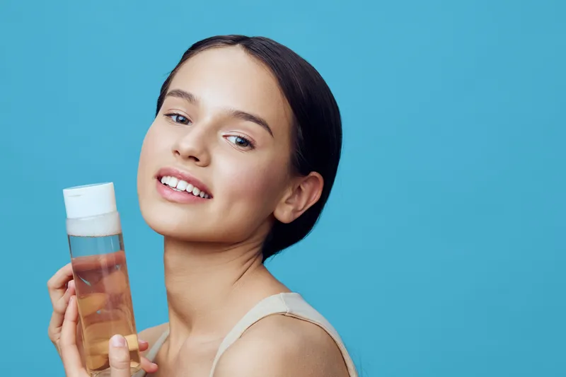 Young woman with glowing skin holding a skincare product against a vibrant blue background, showcasing beauty and self care routine for healthy skin