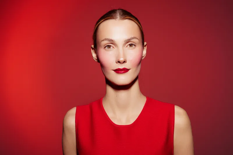 Portrait of confident woman with red lipstick and red dress standing against red background. Minimalist style, beauty concept, fashion and elegance in studio lighting.