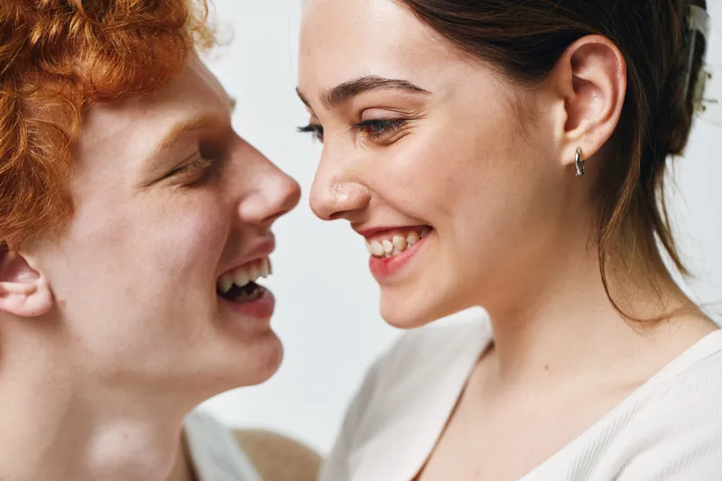 Couple, woman and man smiling closely with happiness and affection, showing emotions and connection, portrait with natural light on white background.