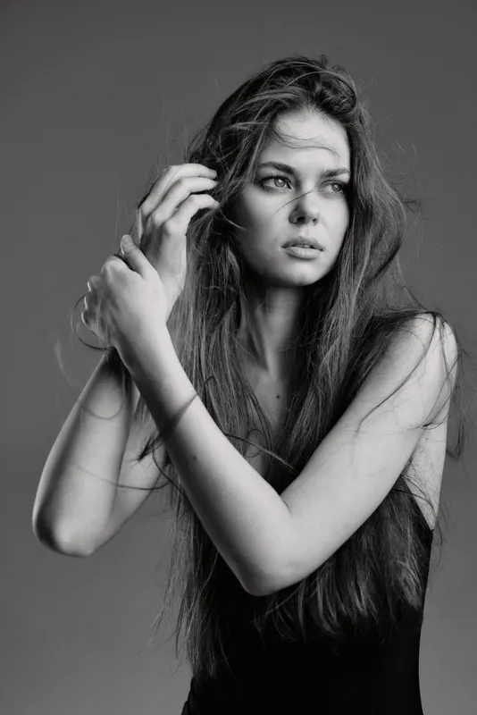 Black and white portrait of a pensive woman with long hair, wearing a sleeveless top, expressing thoughtful emotion and natural beauty.