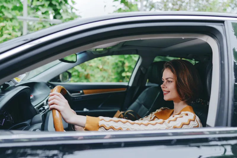 Cheerful woman sits in the driver's seat, hand on the steering wheel, radiating confidence and readiness for a journey.