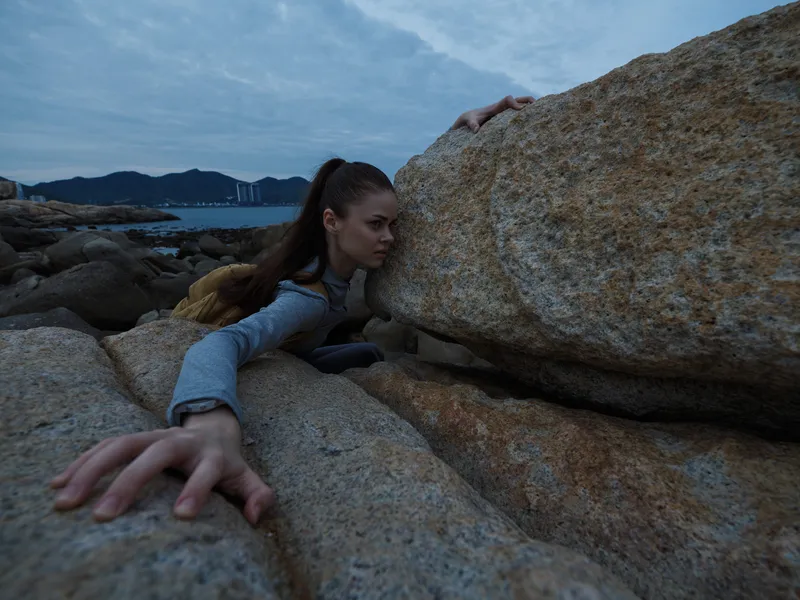 Young female climber struggling against rocky obstacles by the sea, showcasing determination and resilience against challenging elements in nature