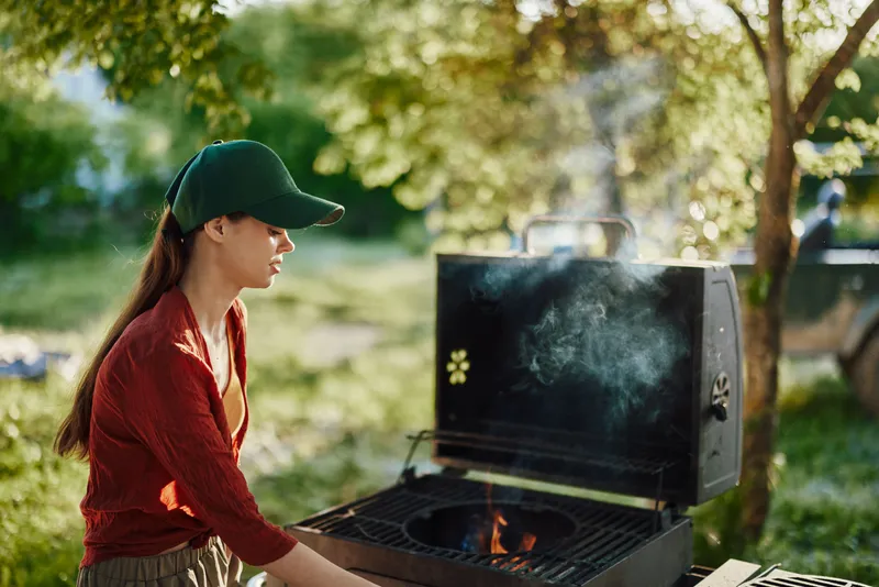 Young woman grilling outdoors in a green park setting, showcasing a relaxed summer vibe and a love for healthy cooking