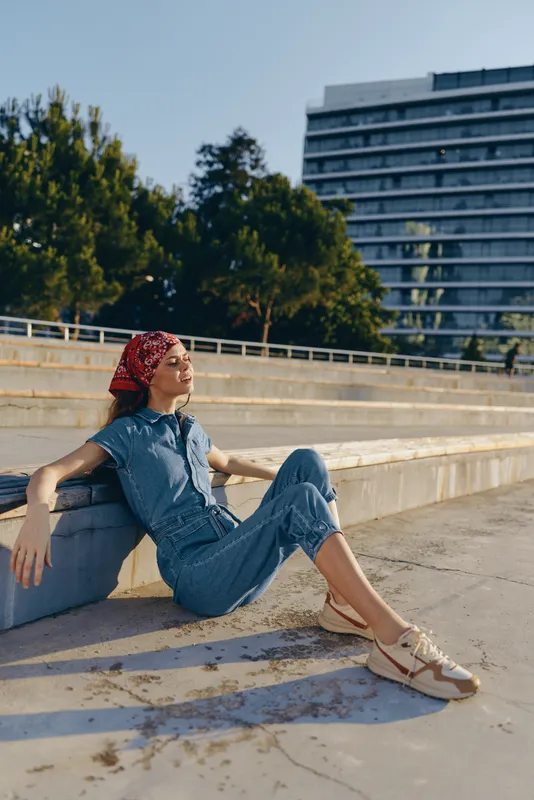 lifestyle woman in modern boho-western denim street style sitting outdoors, relaxed pose, film color effect, casual and stylish urban vibe