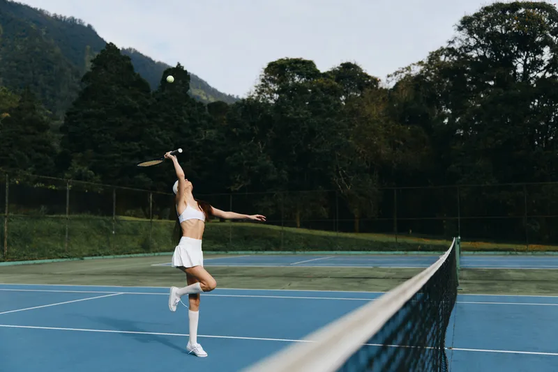 Young female athlete serves the tennis ball on a sunny outdoor court, showcasing determination and focus in her sporty white attire