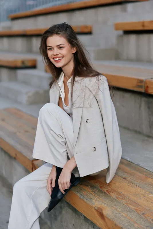 woman smiling in beige stylish suit sitting on wooden benches outdoor casual fashion autumn season business concept