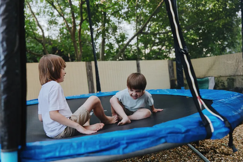 Happy boys playing on a trampoline in a backyard surrounded by greenery, enjoying a fun and playful afternoon together in a sunny environment.