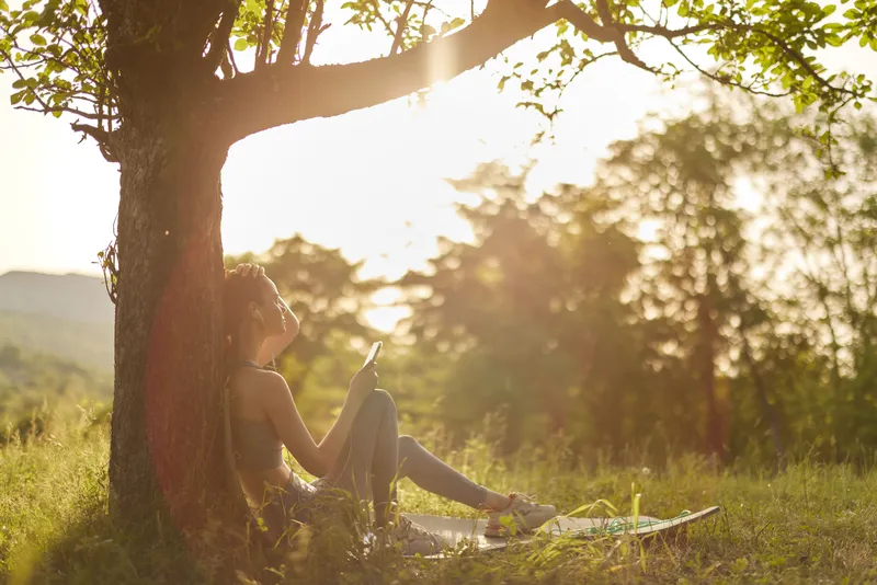 Woman enjoying a peaceful moment under a tree in nature during sunset, embodying tranquility, connection, and harmony with the environment