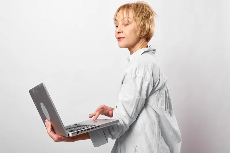 Woman with laptop in studio on white background, side profile, eyes closed, relaxation during work, typing on screen, technology concept, soft light, adult female portrait