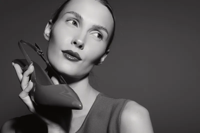 Portrait of a white woman with fair skin holding a high heel shoe near her face in a studio. Concept for fashion, style, and elegance.