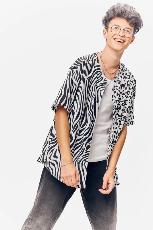 young man smiling wearing patterned short sleeve shirt and glasses standing casually with white background and curly hair, stylish casual summer clothing, modern look