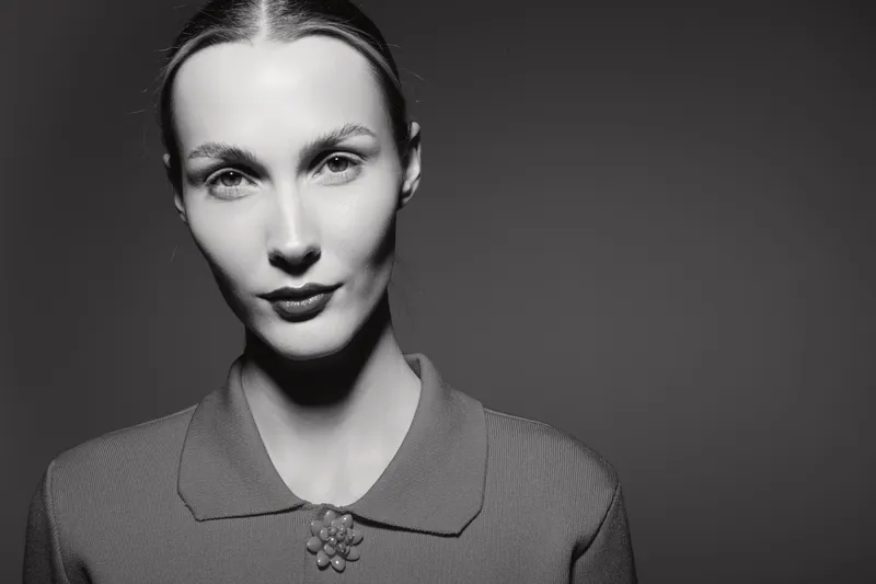 Portrait of a white caucasian woman with pale skin and slicked hair in a textured shirt against dark background. Concept of elegance and fashion.