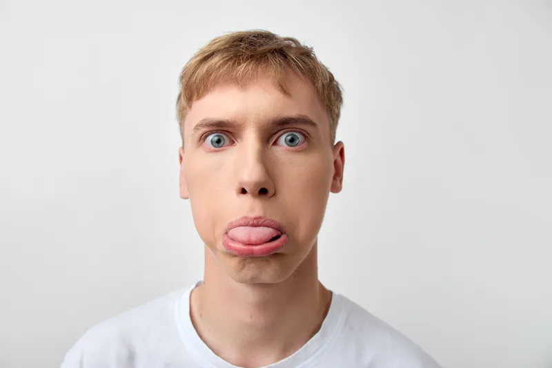 Closeup of a young man with a playful expression sticking out his tongue against a white background, capturing humor, spontaneity, and a bold facial moment