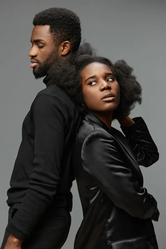 Portrait of a stylish African couple with natural hairstyles in black outfits against a gray background, conveying confidence and connection through body language