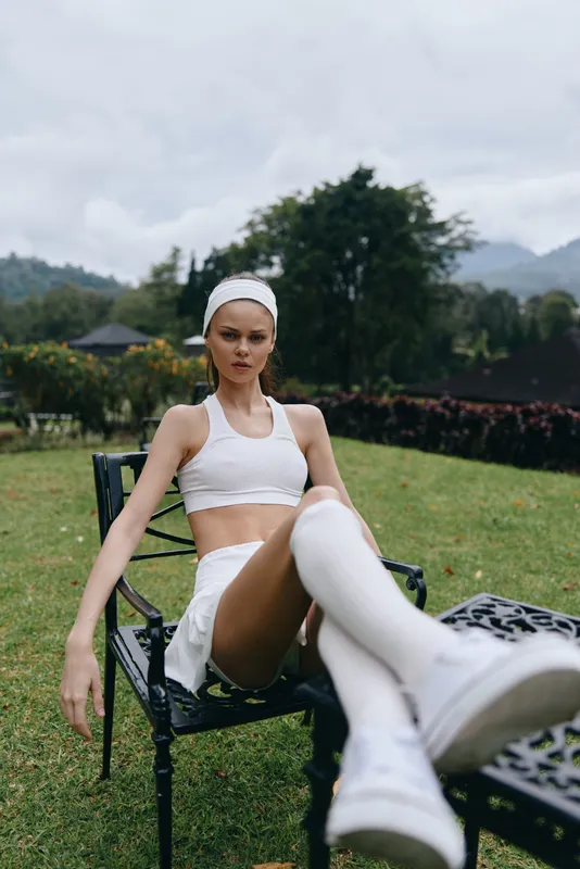 Young model in activewear poses outdoors, showcasing a sporty look with a confident expression amid a lush green background in overcast weather