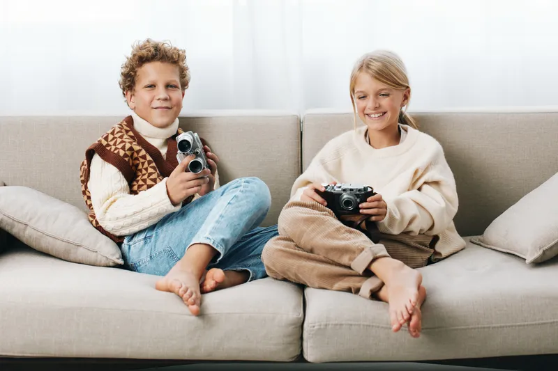 Authenticity shines as two children sit on a cozy couch, sharing cameras in a candid moment that captures play, learning, and everyday life in a warm home.
