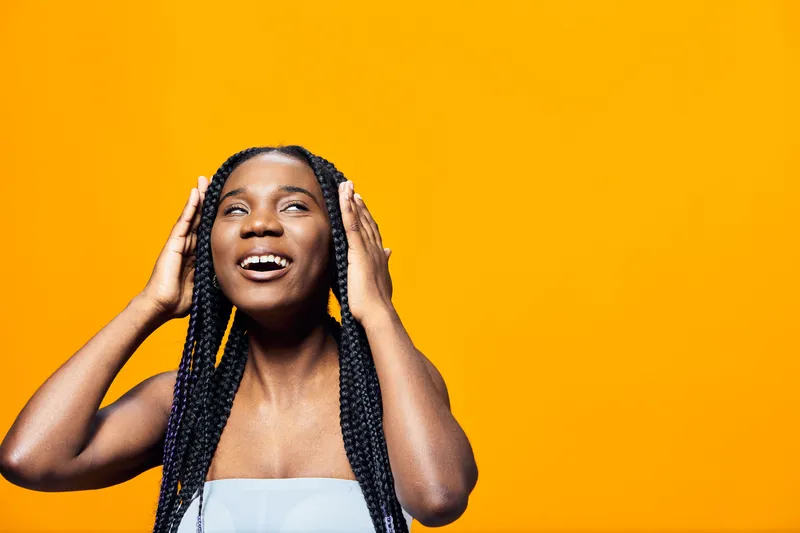 Joyful African woman with braided hair expressing happiness against a vibrant orange background, showcasing the beauty of diversity and confidence