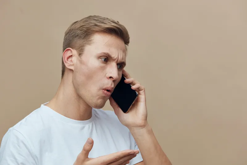 young caucasian man talking serious upset on smartphone isolated beige background emotional gesture concept digital detox mental health gadgets communication