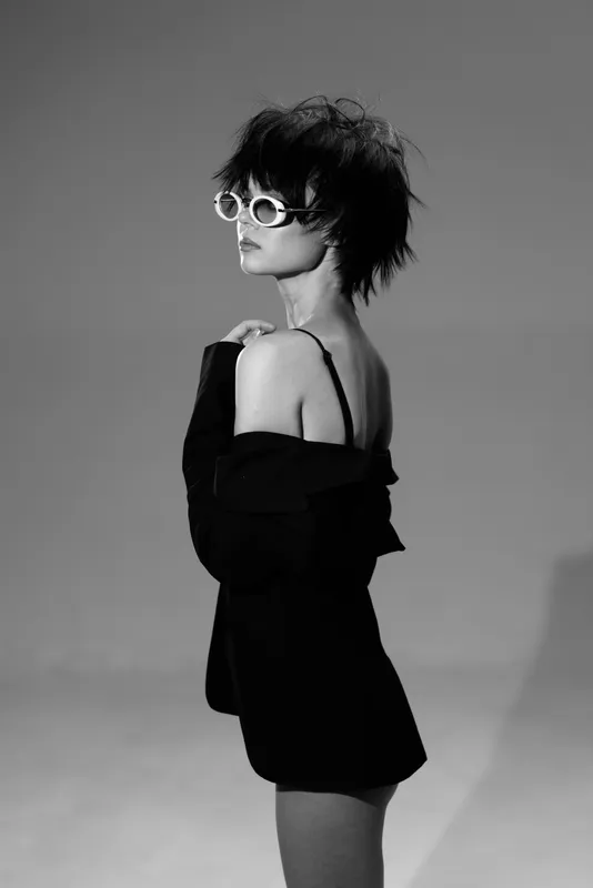 Stylish woman wearing sunglasses and black clothing posing in black and white with a modern edgy look.