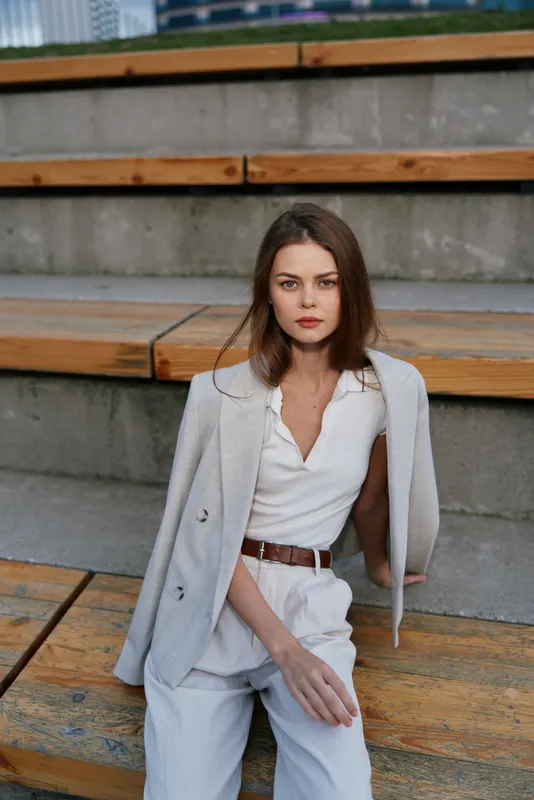 Woman in business casual outfit sitting on urban steps with confident expression in natural light, modern professional style, outdoor environment