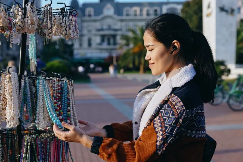 Beads, jewelry, market, outdoor, shopping, colorful, accessories, crafts, display, vendor scene features a female shopper selecting vibrant beads and jewelry from outdoor stalls, sunlight highlights
