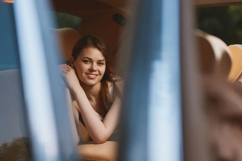 Young woman in a beige outfit smiling softly in a car interior, reflecting joy and warmth in a bright, inviting atmosphere.