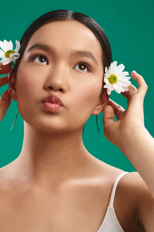 Asian woman with flowers in her hair poses softly against a vibrant green backdrop, creating a fresh, natural look suitable for beauty, lifestyle, and wellness projects.
