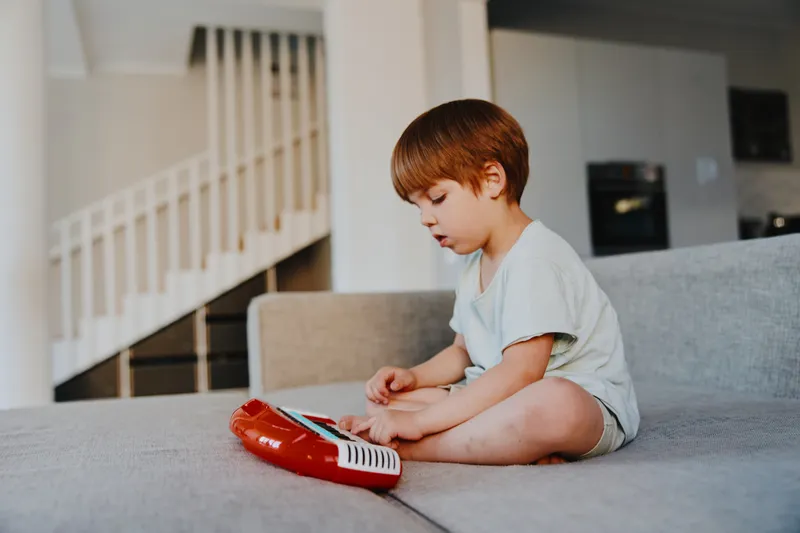 A focused boy engaging with a colorful toy, sitting on a cozy couch in a modern living room, showcasing creativity and playful imagination.
