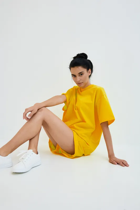 young woman sitting on floor wearing yellow casual outfit with white sneakers, isolated background, natural light, relaxed posture, minimalistic style