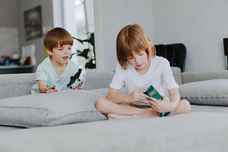 Two children playing together on a cozy sofa in a bright living room, enjoying their toys and sharing laughter in a playful atmosphere.