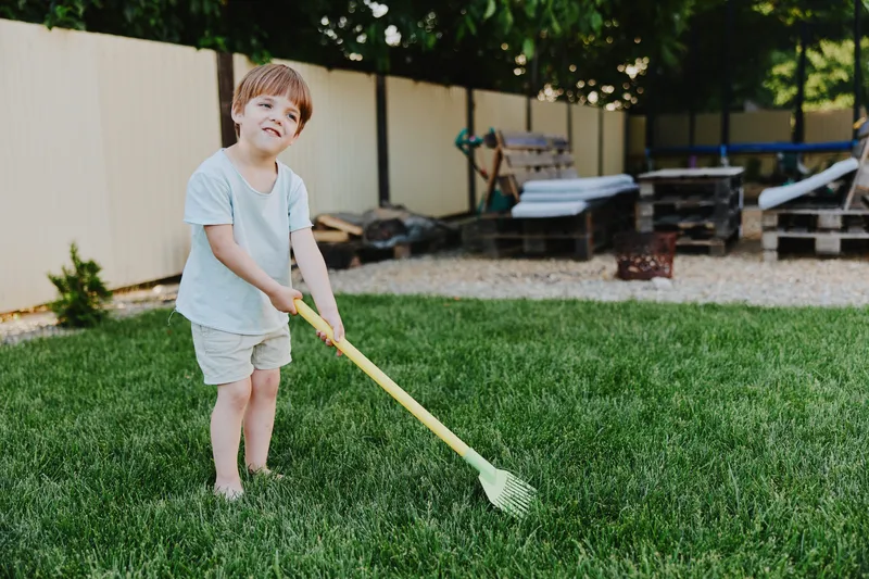 Young boy playing in the garden, enjoying outdoor activities, cheerful atmosphere, sunny day, green grass, child gardening.