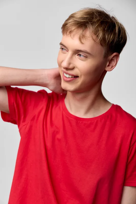 Young man with a bright smile in a red shirt, casual attire, studio shot, and a relaxed pose, capturing a candid moment of cheerful expression and everyday fashion in a clean studio setting.