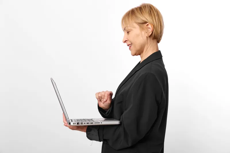 Businesswoman typing on laptop in black suit, senior woman profile on white studio background, focused expression, remote work vibe, copy space office today