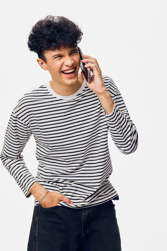 smiling young man talking on smartphone in striped shirt, casual style, curly hair, joyful expression, isolated white background