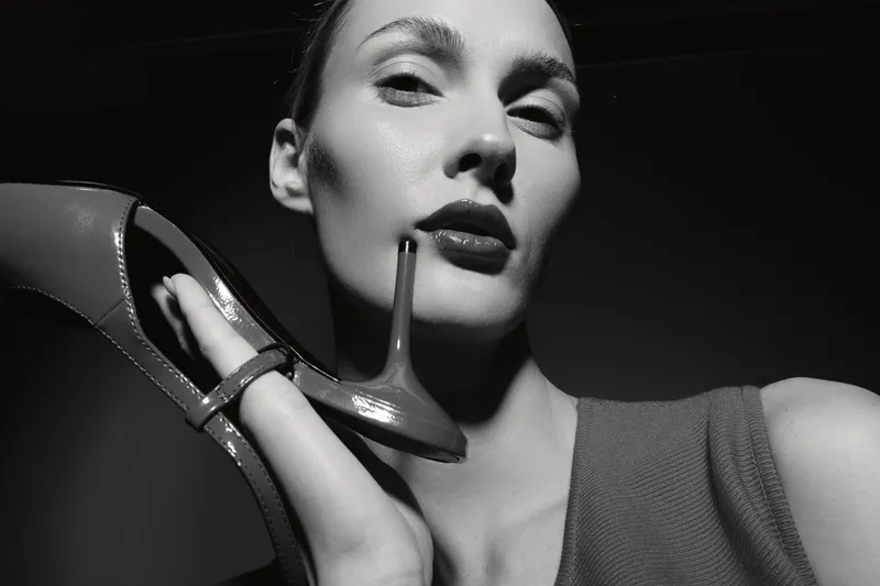 Closeup of a pale white woman with light skin holding a high heel shoe near her face in black and white photo. Concept of fashion and elegance.