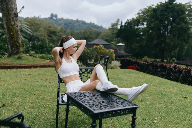 Young athletic woman exercising outdoors in a bright white sports outfit, showcasing a healthy lifestyle with nature in the background