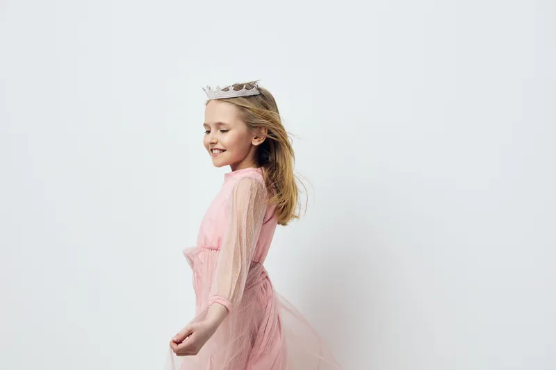 Joyful girl in a pink tulle dress with a crown, dancing happily against a minimalist white background, capturing a carefree and playful moment