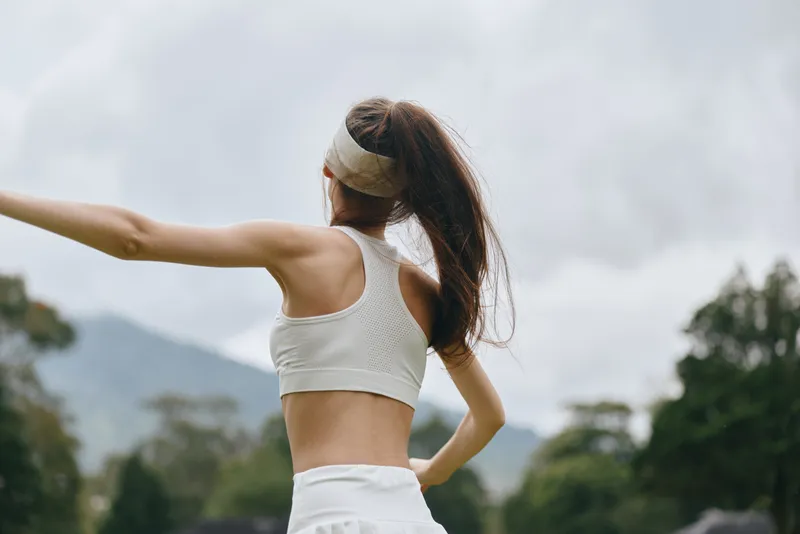 Young athletic woman in a sports bra, enjoying outdoor exercise with an energetic pose, surrounded by nature showcasing a vibrant green background, perfect for fitness inspiration