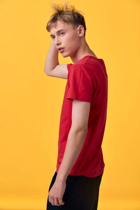 Young man wearing a red shirt poses against a vibrant yellow studio backdrop, creating a bold fashion moment with casual stance, clean lines, and contemporary style suitable for lifestyle and