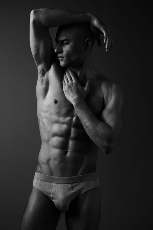 Black and white image of a muscular man striking a pose, showcasing strength and confidence through dynamic body positioning and expressive emotions.