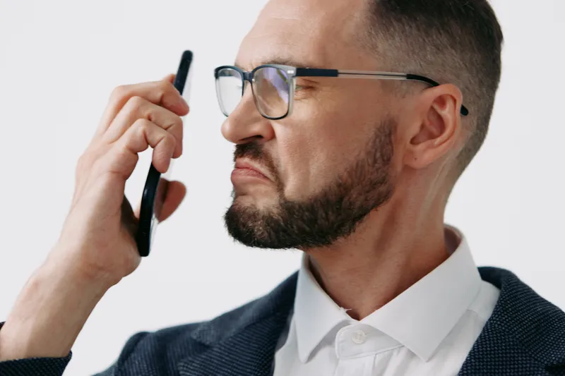 A professional man in business attire holds a phone to his ear on an isolated colored background, displaying a serious, focused expression and strong concentration.