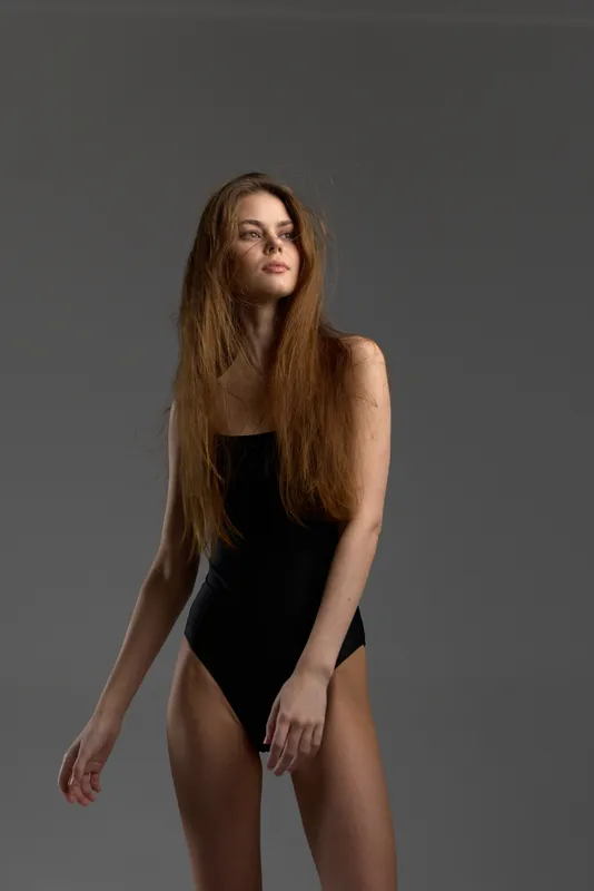 Young woman with long curly hair wearing black swimsuit posing against gray background