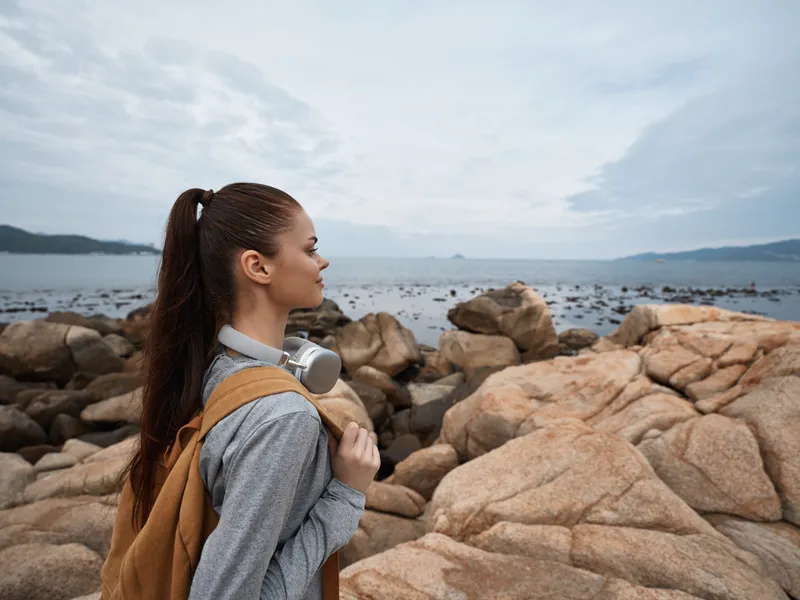 Young woman in casual attire enjoying nature by the seaside, surrounded by rocky landscape, conveying a sense of peace and adventure with a serene expression