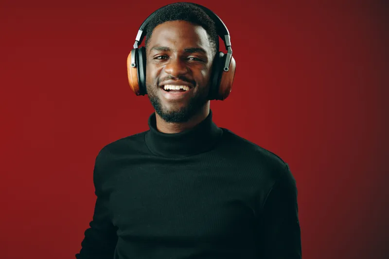 Happy young man with headphones against a red background, expressing joy and passion for music, perfect for concepts related to enjoyment, leisure, and modern lifestyle