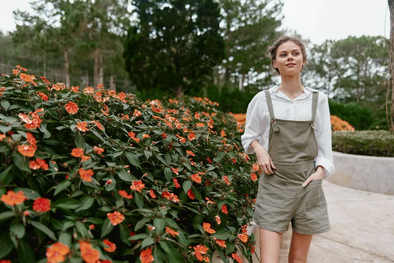 Young woman in casual summer outfit standing among vibrant flowers in a garden, radiating joy and confidence Perfect for themes of nature and lifestyle