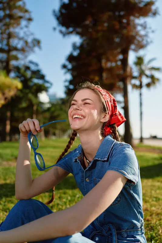 Lifestyle woman in modern boho-western denim street style enjoys sunny outdoor moment with joyful smile, relaxed pose, and vibrant film color tones