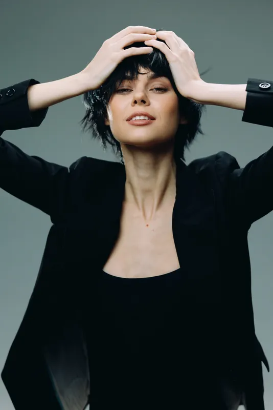 confident woman with short hair posing in black jacket against gray background