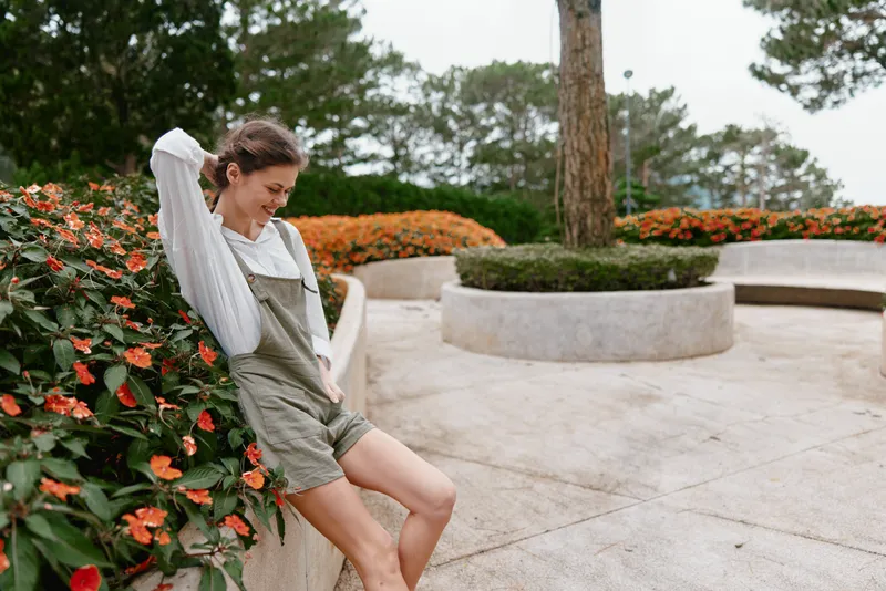 Young woman enjoying a moment of relaxation in a floral park, wearing a casual outfit with emotions of joy and serenity in a bright, spring scene